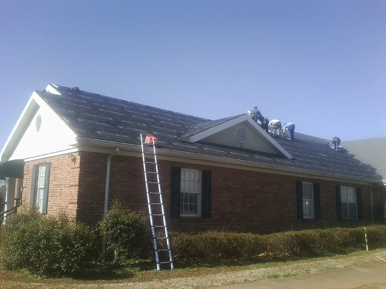 Crew tearing shingles off a brick ranch roof with a ladder set — Emergency Roof Repair work by our crew in Alberton