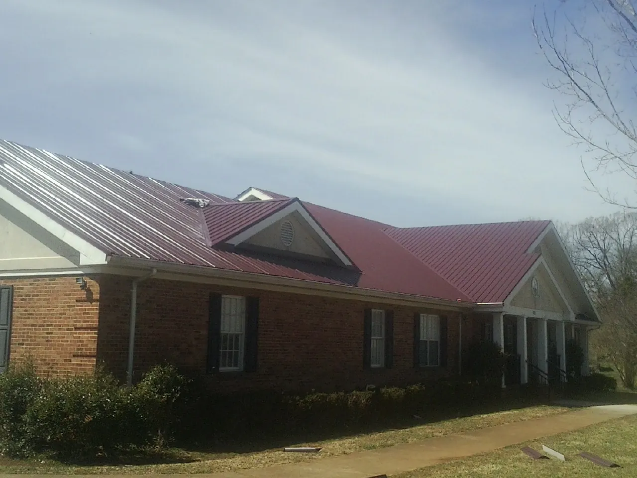 Red metal roof with gabled entries on a long brick building, from a Hail Damage Roof Repair job in Alberton