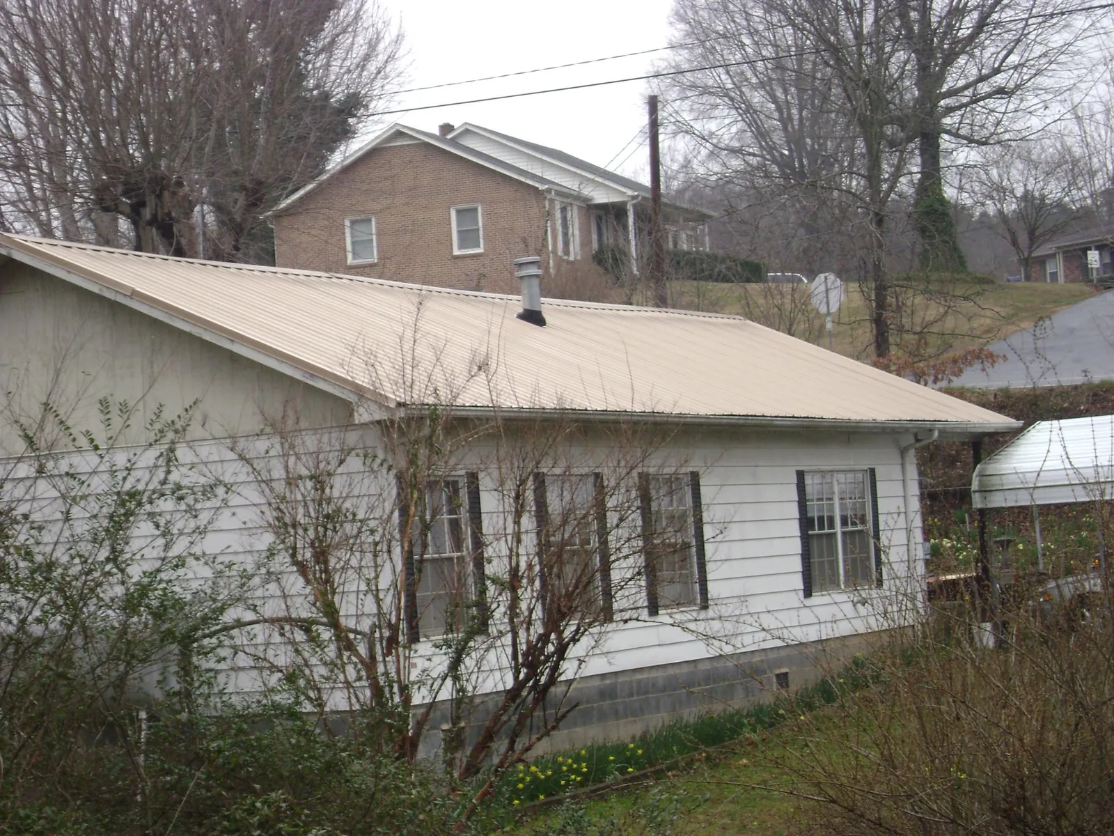 Tan metal roof on a white sided house set into a hillside — Commercial Roofing by Roofing Brothers in Alberton